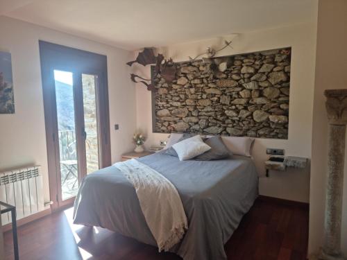 a bedroom with a bed and a stone wall at Hotel Rural L'Ortiga Blanca in Queralbs