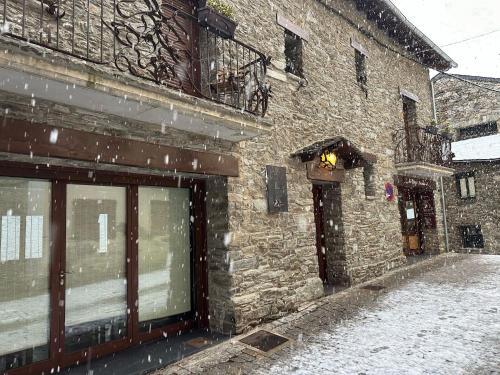 a stone building with snow falling on a street at Hotel Rural L'Ortiga Blanca in Queralbs