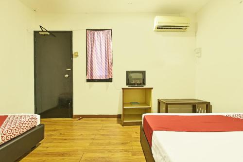 a room with two beds and a television and a door at Hotel O Mini Indah in Kuala Terengganu