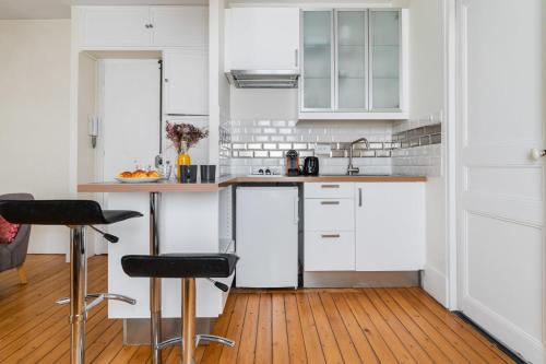 une cuisine avec des placards blancs et des tabourets de bar noirs dans l'établissement Studio cosy proche Opera Bastille paris 11, à Paris