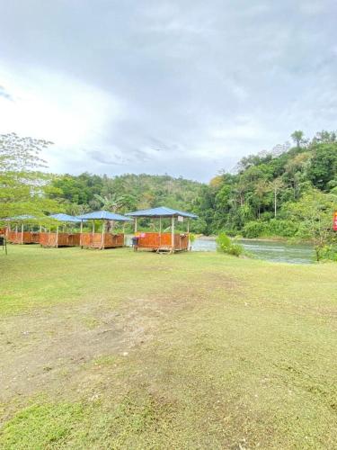 a field with several tables and umbrellas next to a river at Hotel O Disan Baang Kiulu in Kiulu