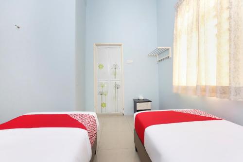 two beds in a room with white walls and red sheets at Hotel O Come Inn Premium in Kuala Terengganu