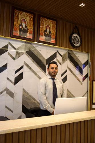a man standing in front of a desk with a laptop at الموج للشقق الفندقية in Falaj al Qabāʼil