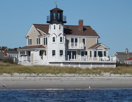 a large white house with a lighthouse on the beach at West Yarmouth - Luxury Oceanfront Vacation Home in Yarmouth