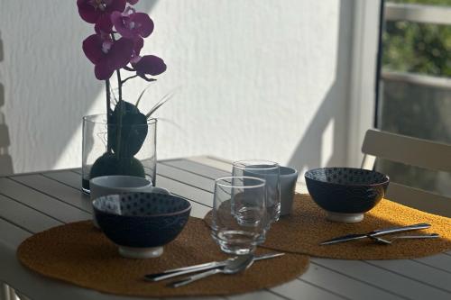 Una mesa con cuencos y vasos y un jarrón con flores. en T2 vue mer climatisé wifi & refait à neuf idéalement situé à Ajaccio, en Ajaccio