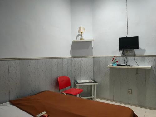 a room with a bed and a red chair and a television at Hotel O Baruga Makassar in Makassar