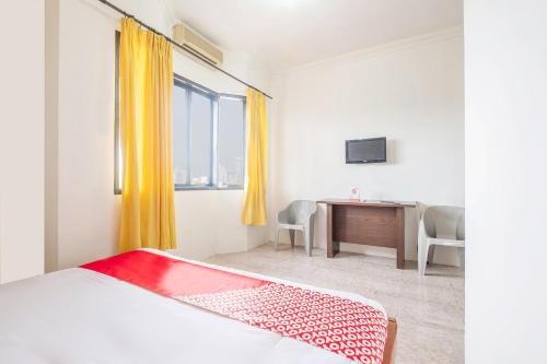 a bedroom with a bed and a desk and a window at Hotel O Transit 2 in Makassar