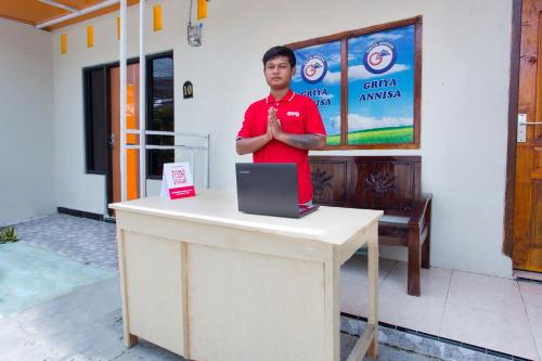 a man standing next to a table with a laptop at Hotel O Griya Annisa in Tegal