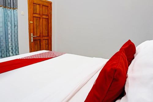 a bed with red and white sheets and a wooden door at OYO 91599 Penginapan Mutiara Madiun in Madiun