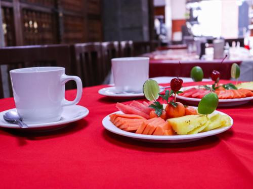 a table with plates of fruit and cups on a red table cloth at Hotel Frances in Guadalajara