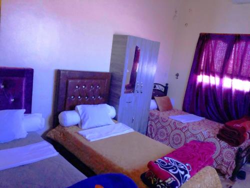 a bedroom with two beds and purple curtains at Tata Guest House in Tatta