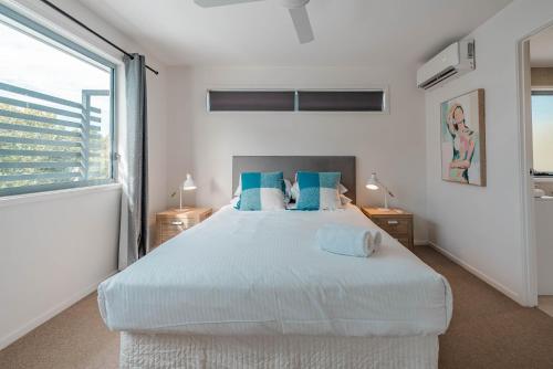 Un dormitorio blanco con una cama grande con almohadas azules. en Suncoast Beach Drive Townhouses, en Yaroomba