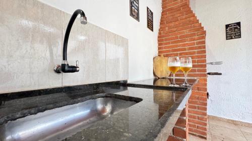 a sink with a glass of wine next to a brick wall at Casa terrea perfeita para familias 100 m da praia do Arpoador, com piscina, churrasqueira, ar condicionado e 4 quartos in Peruíbe