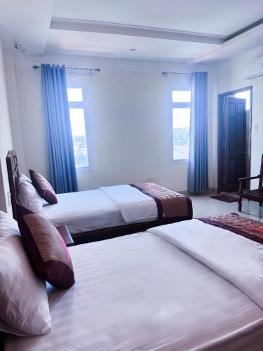 two beds in a room with blue curtains at An Thái Hotel in Kon Tum