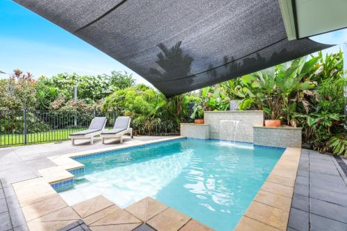 a swimming pool with a patio umbrella and two chairs at Villa Blue - Coastal Family Escape in Palm Cove