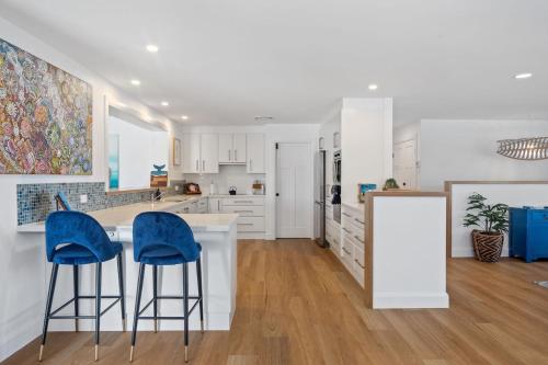 a kitchen with white cabinets and blue bar stools at Gawura in Burrill Lake
