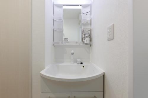 a white bathroom with a sink and a mirror at BALOH Wadamisaki in Kobe