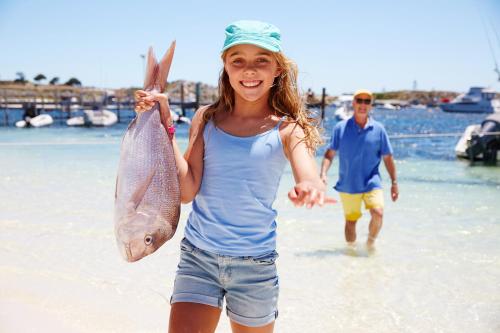 a young girl holding up a fish on the beach at Stay Rottnest in Rottnest Island