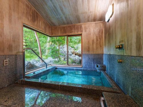 a bathroom with a hot tub with a window at 旅亭 半水盧 in Unzen