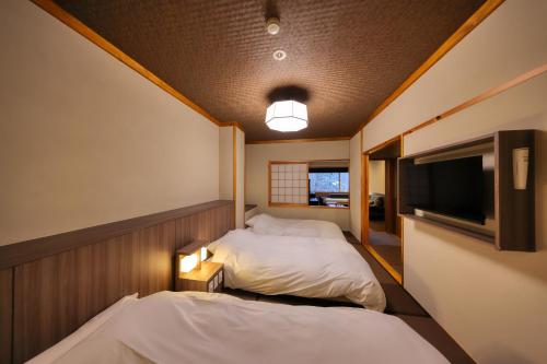 two beds in a small room with a tv at Miyama Ouan Kyoritsu Resort in Takayama