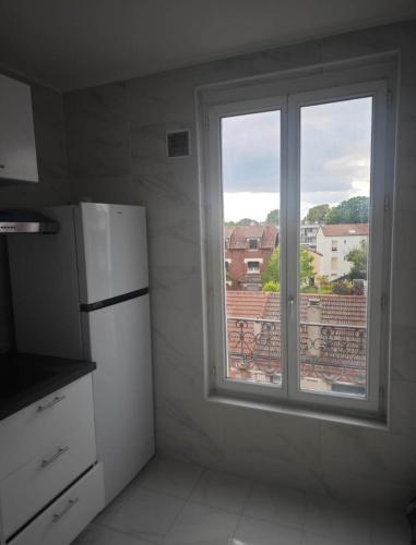Il comprend une cuisine avec une fenêtre et un réfrigérateur blanc. dans l'établissement Séjour en ville, à Aubervilliers