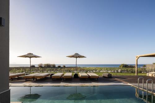 a pool with benches and umbrellas and the ocean at Villa Aya - Coastal Villa, Minimalist Elegance by etouri in Stavromenos