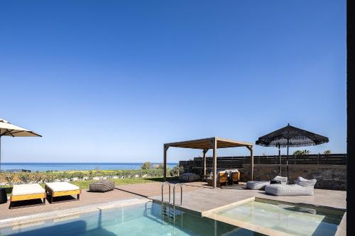 a swimming pool with chairs and umbrellas next to the ocean at Villa Aya - Coastal Villa, Minimalist Elegance by etouri in Stavromenos