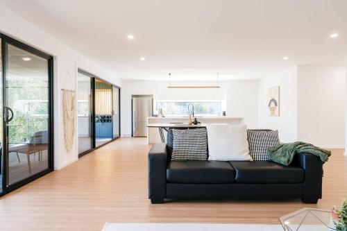 a living room with a black couch and a kitchen at Tree Top Treasure Itas in Kings Meadows
