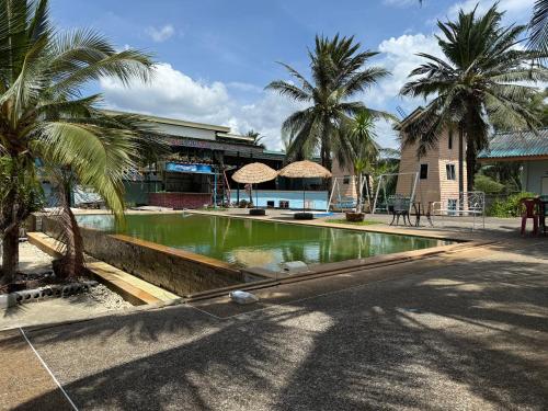 a swimming pool with palm trees in front of a building at Sai Rung Farmstay สายรุ้ง ฟาร์มสเตย์ in Ban Huai Yung