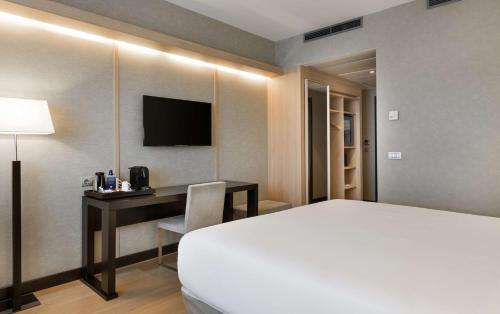 a hotel room with a bed and a desk with a television at NH Madrid Ribera del Manzanares in Madrid