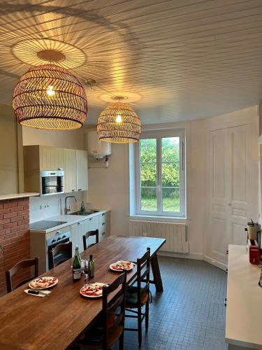 une cuisine avec une table en bois, des chaises et deux lumières dans l'établissement Maison de famille au cœur du bocage normand, à Besneville