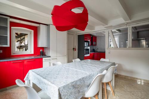 une cuisine avec une table, des chaises blanches et des armoires rouges dans l'établissement Renovated house with garden -20min from Strasbourg, à Blaesheim