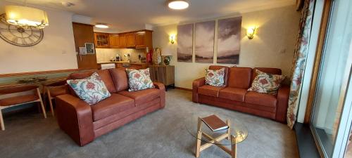a living room with two brown couches and a kitchen at Loch Rannoch Highland Club in Kinloch Rannoch