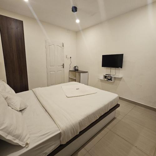 a white bedroom with a bed and a television at Heres Haut Residency in Ernakulam