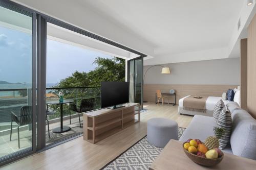 a room with a living room with a television and a balcony at Andaman Beach Hotel Phuket - Handwritten Collection in Patong Beach