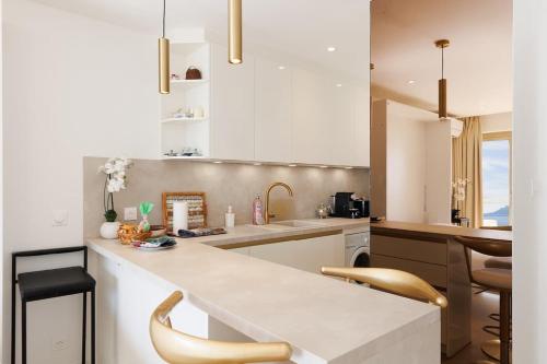 une cuisine avec des placards blancs et un comptoir avec des chaises dans l'établissement Sur la Croisette studio neuf, à Cannes