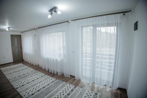 a bedroom with white curtains and a bed in front of a window at Boierița Home Stay in Fundu Moldovei