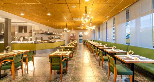 a restaurant with wooden tables and green chairs at PLAZA INN Regensburg in Regensburg