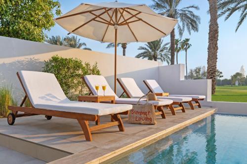 a row of lounge chairs and an umbrella next to a swimming pool at Elara & Golf Villas - curated by Park Hyatt Dubai in Dubai