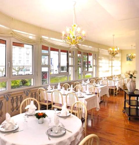 un restaurant avec des tables et des chaises blanches et des fenêtres dans l'établissement Hôtel Roc de Massabielle, à Lourdes