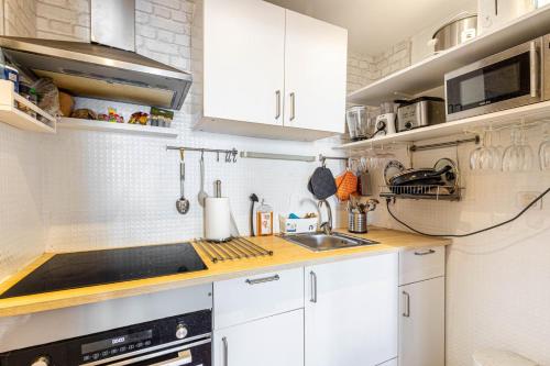 une cuisine avec des armoires blanches et un évier dans l'établissement GuestReady - Cosy studio near Arc de Triomphe, à Paris