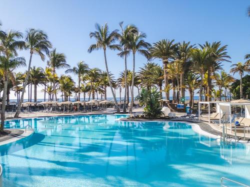 a swimming pool with palm trees and the ocean at Hipotels La Geria in Puerto del Carmen