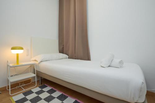 ein Schlafzimmer mit einem weißen Bett mit einer Lampe und einem Tisch in der Unterkunft Park Guell in Barcelona