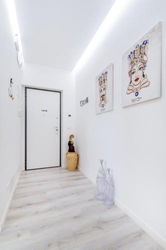 a white hallway with a door and paintings on the walls at Heart City Rooms in Catania