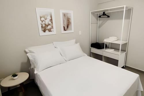 a white bedroom with a white bed and a table at 2 quartos com ar e garagem in Londrina