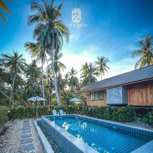 a swimming pool in front of a house with palm trees at Mucoco Khanom in Ban Thong Tanot