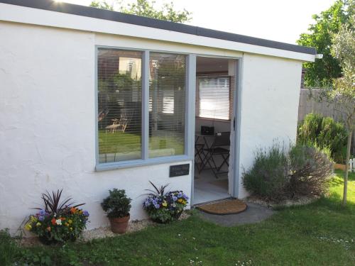 a white house with a window and some plants at The Studio Christchurch B&B Luxury Garden Room in Christchurch