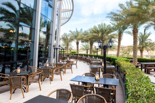 an outdoor patio with tables and chairs and palm trees at Novotel Abu Dhabi Gate in Abu Dhabi