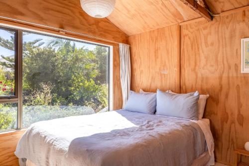 un lit dans une chambre avec une grande fenêtre dans l'établissement Tranquility Cottage, Oneroa - Be My Guest Waiheke, à Waiheke Island