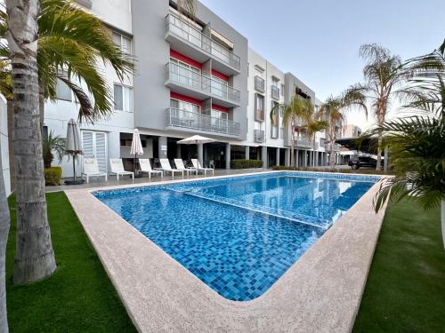 a swimming pool in front of a building with palm trees at Departamento con BONITA VISTA , BALCÓN y ALBERCA !! en CERRITOS - 406 A - in Mazatlán